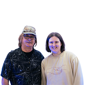 A photograph of CHAOS Radio presenters Nicola and Stephan from the Creature Feature Show; Nicola (female) is wearing a beige jumper that features a printed fine-line logo of a human hand holding an animal paw. Stephan (male) is wearing a black tshirt that features a white cobweb design all over, black-framed glasses, and a grey/beige cap.