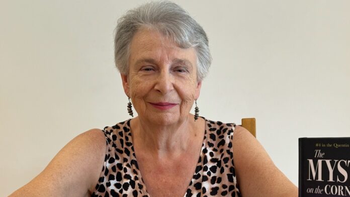 CHAOS Radio Newswave - St Austell Author Christine McHaines sits facing the camera waring a leopard-print top and long silver earrings - almost off-camera to her right is her book.